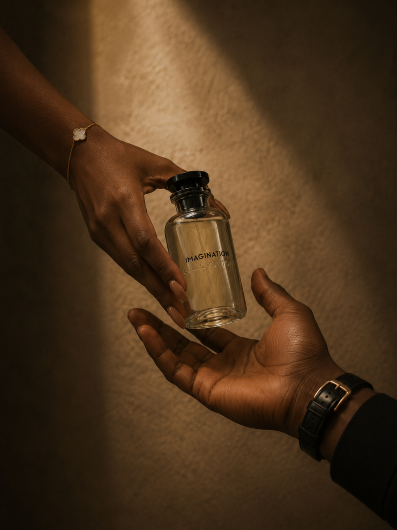 Two hands exchanging a clear Louis Vuitton Imagination perfume bottle against a warm brown background.
