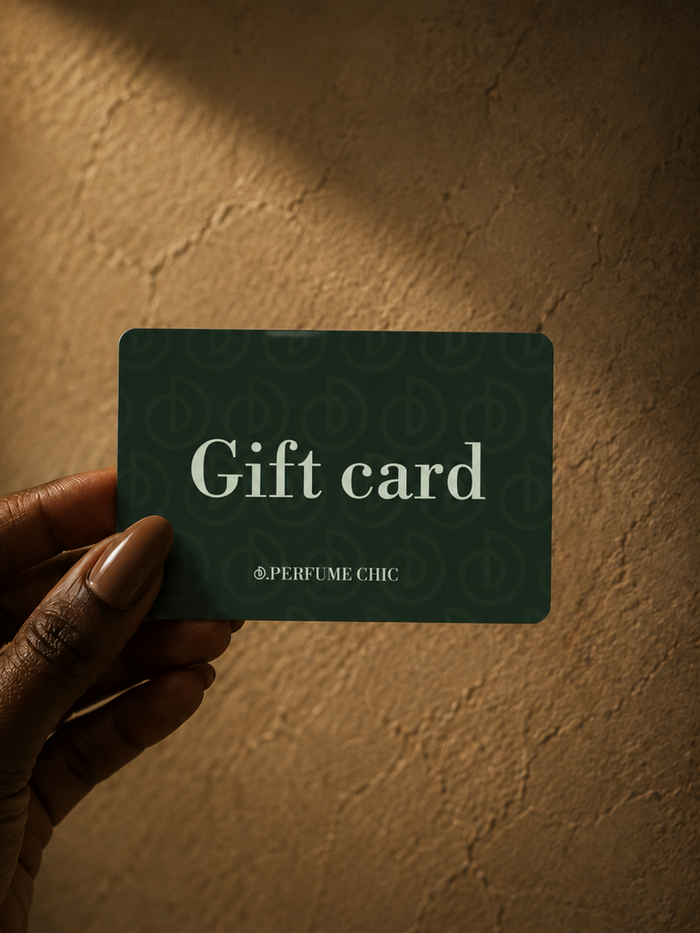 A hand holds a dark green DPerfumeChic gift card reading "Gift card" against a warm textured wall.