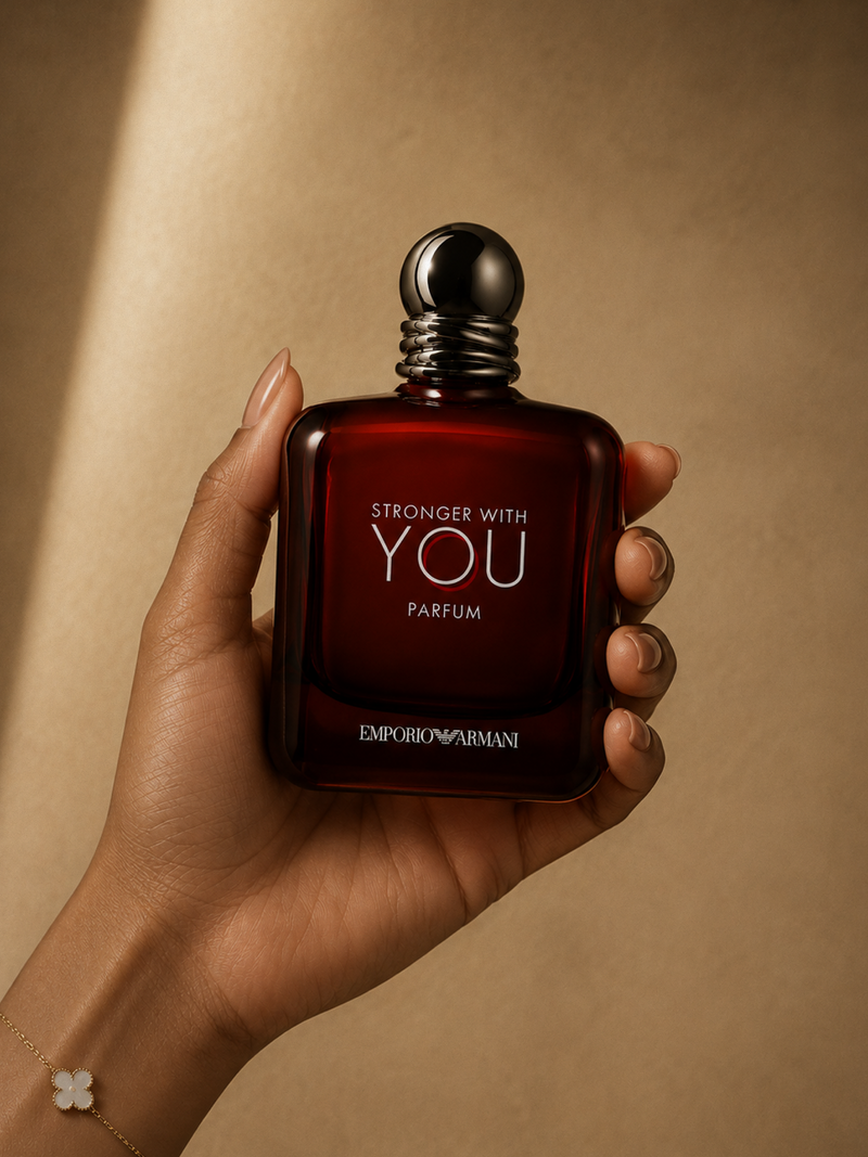 A hand holding a bottle of Emporio Armani Stronger With You Parfum against a warm beige background.